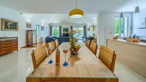 A spacious dining area with a long wooden table, multiple chairs, and a central vase with flowers.