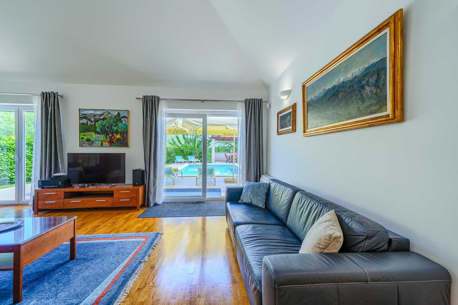 Un salon moderne avec un canapé en cuir, un téléviseur à écran plat, des meubles en bois et une vue sur un espace piscine extérieur.