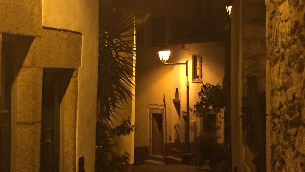 A narrow alleyway with stone walls, a lamp post, and a door at the end.