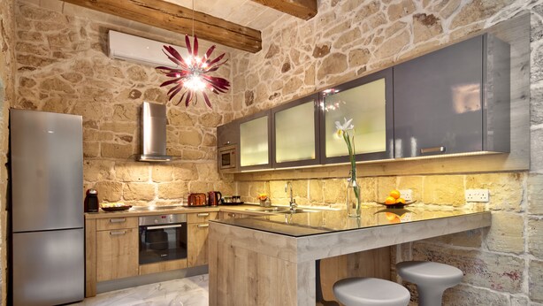 A kitchen with a stone wall, wooden cabinets, a stainless steel refrigerator, and a marble floor. - Highly Renovated Ta Rozamari Character House With Pool And Hot Tub (Zejtun)
