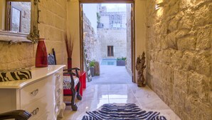 A narrow hallway with stone walls, a zebra-patterned rug, a wooden chair, a white dresser, and a mirror on the left. - Highly Renovated Ta Rozamari Character House With Pool And Hot Tub (Zejtun)