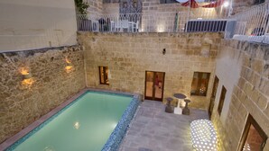 A stone courtyard with a swimming pool, outdoor seating, and a balcony with a railing. - Highly Renovated Ta Rozamari Character House With Pool And Hot Tub (Zejtun)