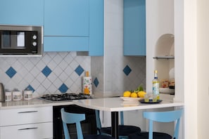 A kitchen with blue cabinets, a microwave, a gas stove, and a dining area with two blue chairs.
