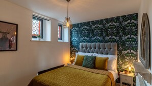 Ein Schlafzimmer mit einem großen Bett, einem gepolsterten Kopfteil, einem Fenster mit Blick und einer Wand mit grünem Muster.