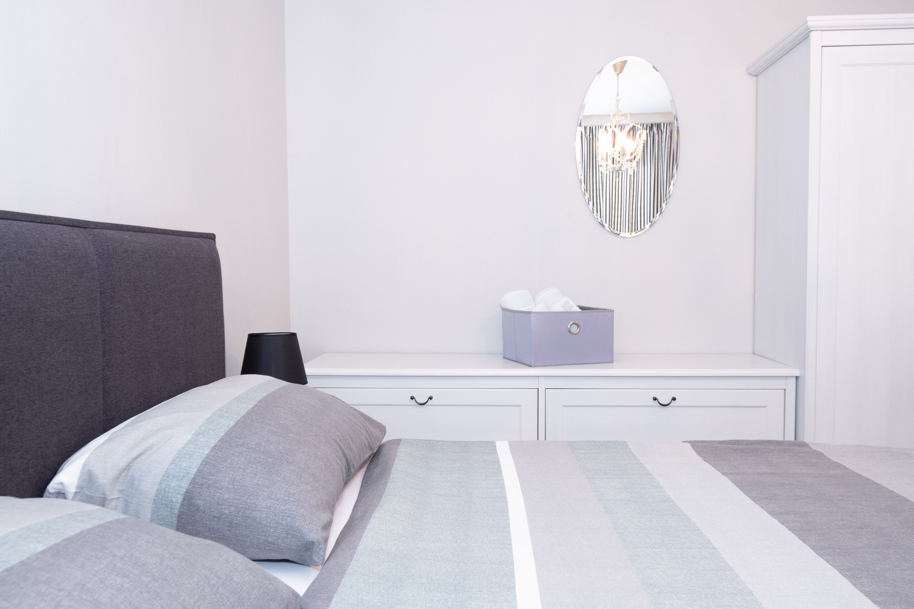 A bedroom with a bed, bedside table, lamp, and a mirror on the wall.