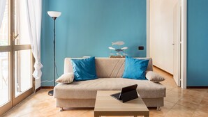 Un salon avec un canapé beige, une table basse sur laquelle se trouve un ordinateur portable, un lampadaire et une sculpture décorative représentant un poisson.