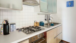 Une cuisine avec des carreaux blancs, une cuisinière à gaz, une machine à café et un évier.