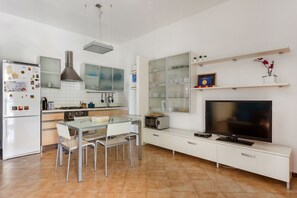 A modern kitchen with a dining area, white cabinetry, a flat-screen TV, and a microwave.