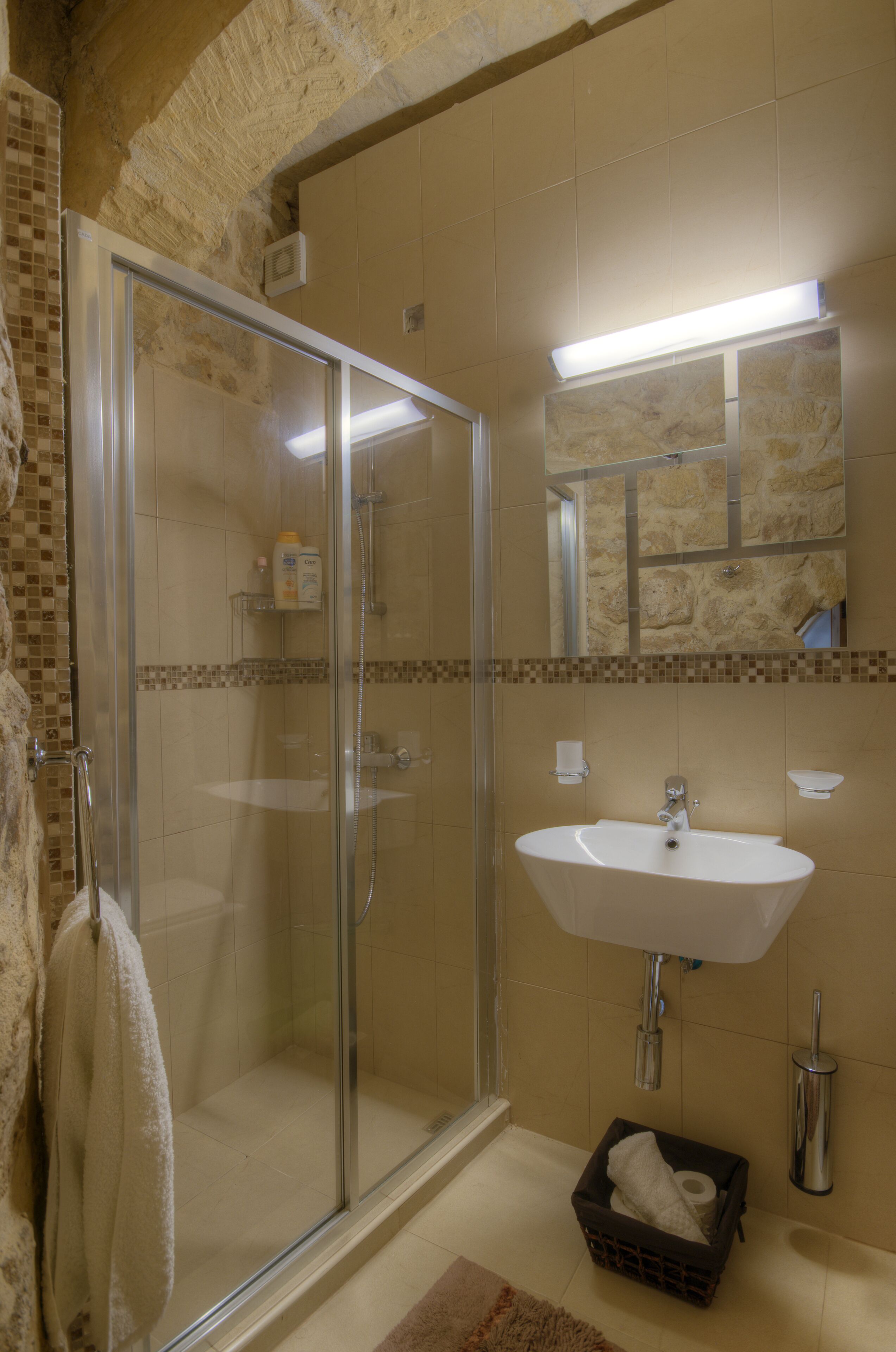 Un baño con cabina de ducha de vidrio, lavamanos y espejo.