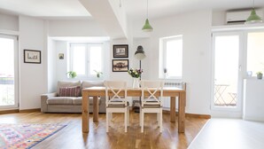 Un salón luminoso con una mesa de comedor de madera, dos sillas, un sofá y una alfombra colorida.