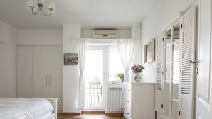 Un dormitorio con cama, cómoda, radiador y ventana con cortinas.
