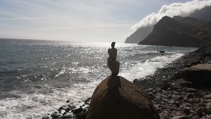 Una costa rocosa con un gran bolo de piedra en primer plano y una montaña al fondo.