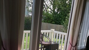 A deck with a table and chairs, a white railing, and a view of a backyard with a fence and greenery.