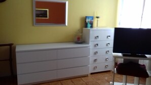 Habitació amb un armari blanc, una televisió sobre un moble i una fotografia emmarcada a la paret.