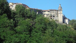 Edifici històric amb diversos nivells i una torre campanar destacada, envoltat de vegetació densa.
