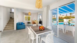 A spacious living area with a dining table, white chairs, a blue sofa, and a large window overlooking a pool. - This amazing luxury villa is located in the heart of Protaras just 4 minutes walk to the Main Str (Protaras)