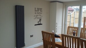 A dining area with a wall decal stating "LIFE is better at the Beach!" and a view of a wooden deck outside. - Chloe Cottage - Family friendly fishermans cottage close to the beach and harbou (Whitstable)