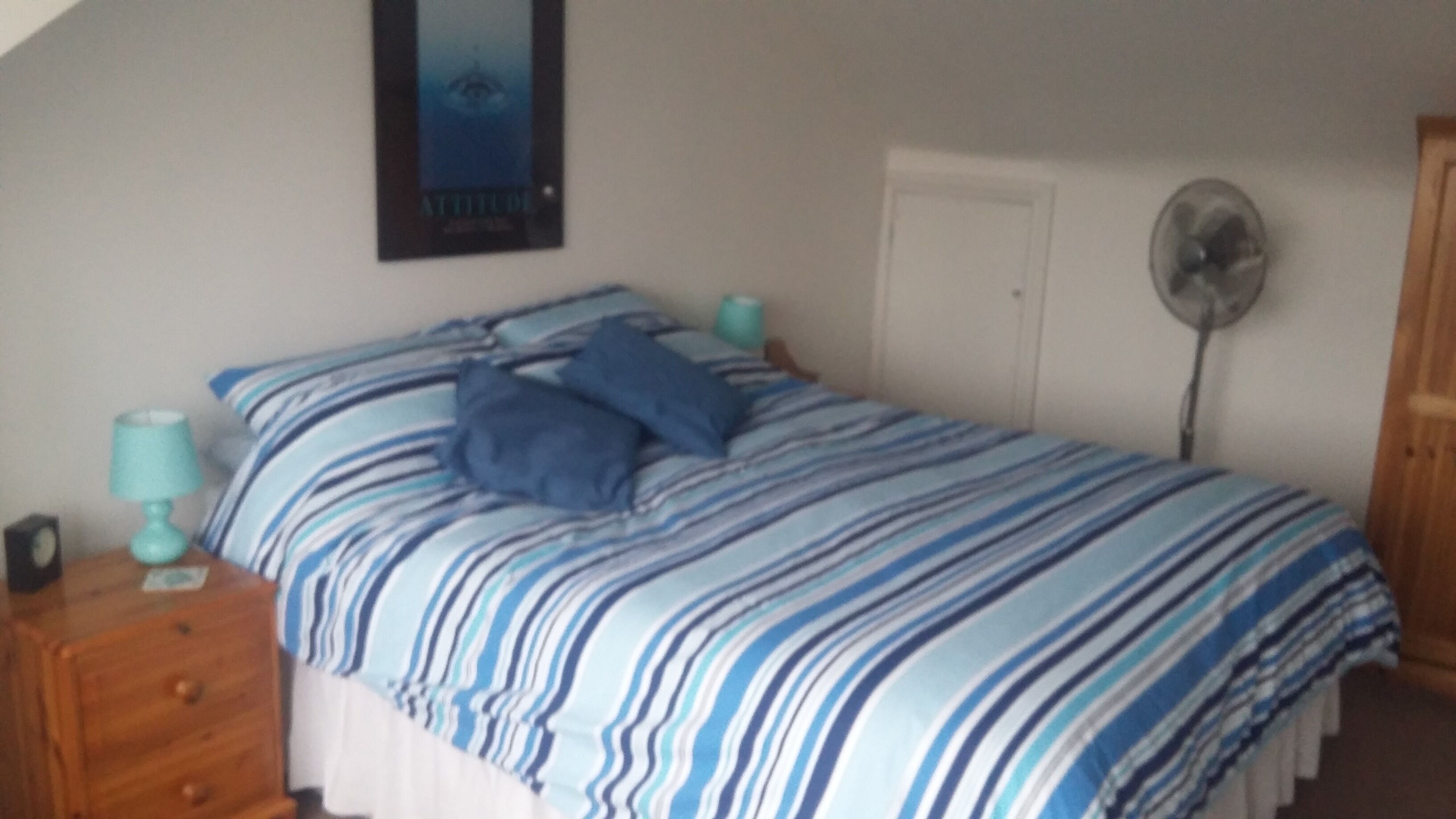 Une chambre à coucher avec un lit, deux tables de chevet, un ventilateur fixé au mur et une porte.