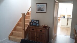 A staircase leading to a balcony, a wooden cabinet with framed pictures, and a door to an outdoor area. - Chloe Cottage - Family friendly fishermans cottage close to the beach and harbou (Whitstable)
