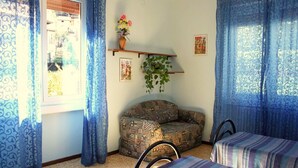 Quarto com sofá estampado, duas camas listradas, planta pendente e janela com vista.