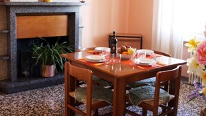 Uma sala de jantar com lareira, mesa posta para quatro pessoas e um vaso com planta.