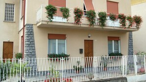 Um edifício de dois andares com varanda decorada com flores vermelhas, fachada de pedra e cerca de pedra em primeiro plano.