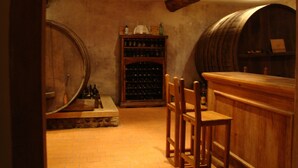 Ein Weinkeller mit Holzfässern, einem Weinschränkchen und einer Bar mit Sesseln.