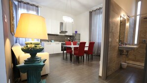 A modern kitchen with white cabinets, a dining area with red chairs, and a bathroom with a large mirror and bathtub.