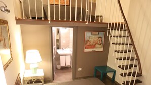 A bedroom with a large bed, a staircase, a bathroom, and a small table.
