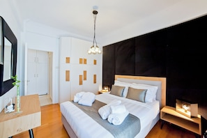 A modern hotel room with a large bed, a bedside table, a desk, and a wardrobe.