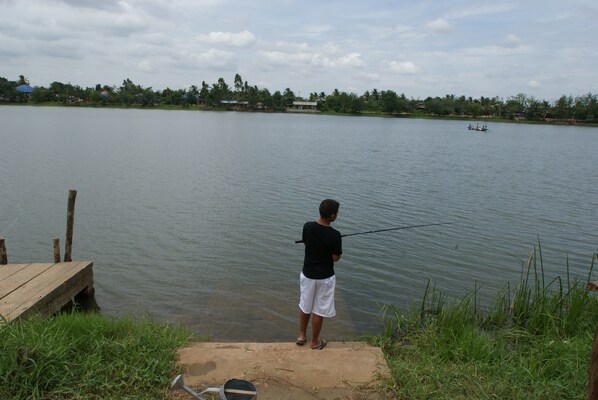 A person fishing by a calm lake with a wooden dock and a distant boat. - A fantastic calm big house with a great lakeview! (Ratchasima)