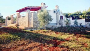 Una casa de piedra con una pérgola roja, un pequeño árbol y un jardín.