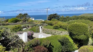 A coastal landscape with a view of the sea, lush greenery, and a white building with a gate. - Clemens Beach House, Sea Views, Private Lane, Crantock, Sleeps 4. (Crantock, Cornwall)