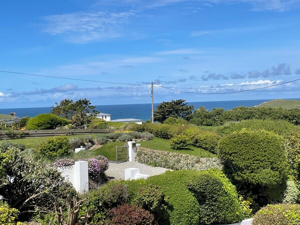 A coastal landscape with a view of the sea, lush greenery, and a white building with a gate.