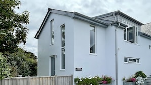 A two-story house with a grey exterior, a wooden fence, and flower planters in front. - Clemens Beach House, Sea Views, Private Lane, Crantock, Sleeps 4. (Crantock, Cornwall)