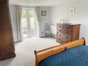 Un dormitorio con cama, cómoda, silla y vistas a un espacio exterior a través de un ventanal.