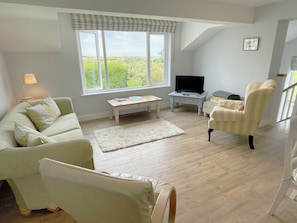 Una sala de estar con sofá, sillón y televisor sobre un mueble.
