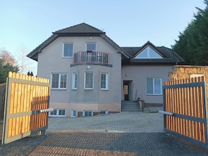 Ein zweistöckiges Haus mit Balkon, geschlossenem Eingangsbereich und gepflasterter Auffahrt.