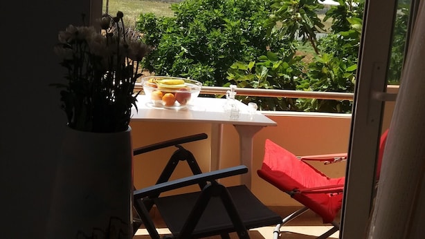 A balcony with a table, chairs, and a vase of flowers.