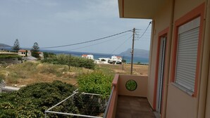 A balcony with a view of the sea, a round window, and a door with a shutter.