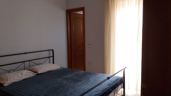Une chambre avec un lit simple, une porte en bois et une fenêtre avec des rideaux.