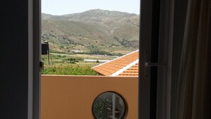 A room with a bed, a window with curtains, and a view of a mountainous landscape.