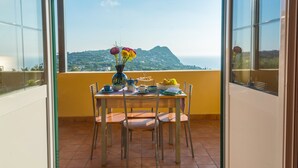 Un balcón con una mesa dispuesta para el desayuno, un florero con flores y vistas a un paisaje montañoso.
