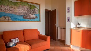 Una sala de estar con un sofá, un cuadro de una escena costera y una cocina con armarios color naranja.