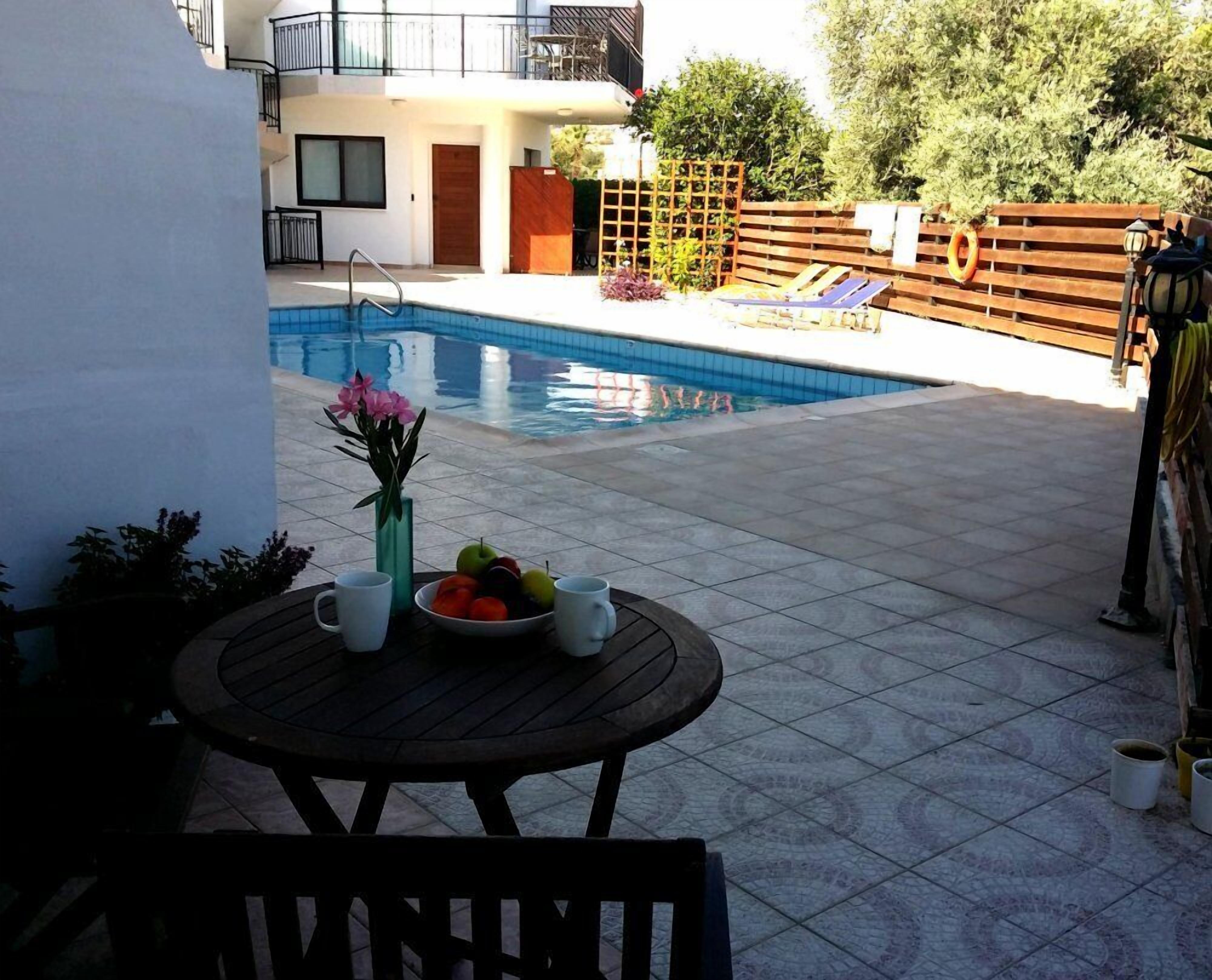 Zona de piscina con mesa, sillas y un cuenco de fruta.
