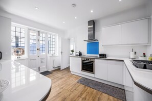 A modern kitchen with white cabinetry, a stainless steel range hood, and a built-in oven.