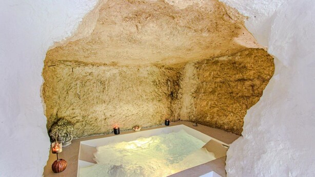 Une pièce aux murs de pierre, dotée d’une baignoire, de bougies et d’un objet décoratif.