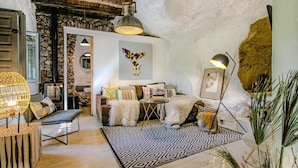 Un salon chaleureux avec un mur en pierre, un tapis à motifs, une table basse en bois et un luminaire suspendu.