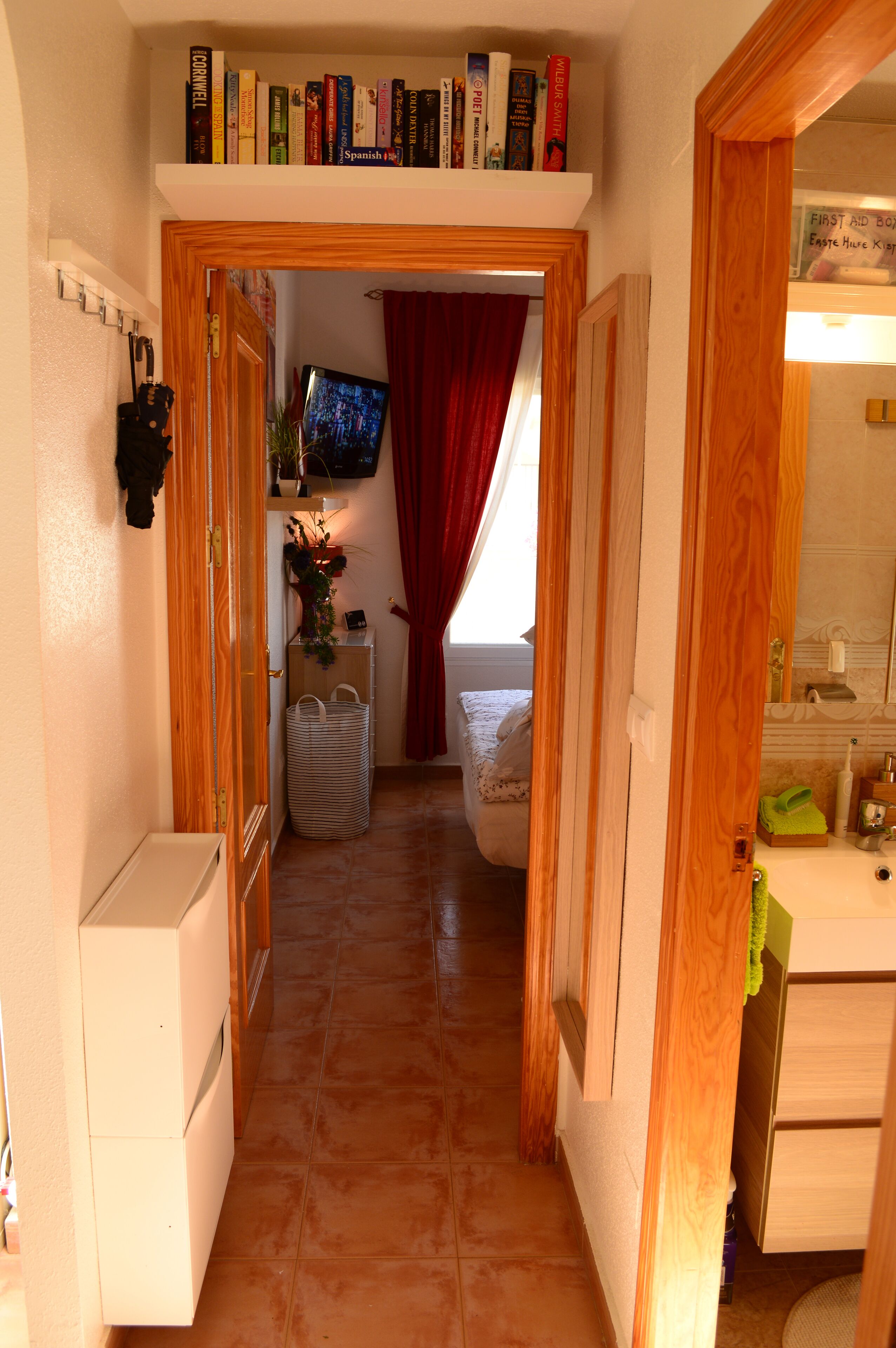 Un pasillo estrecho que lleva a un dormitorio con televisión, cama y un baño visible a través de una puerta abierta.