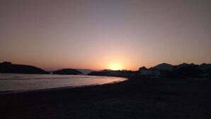 Ein Strand bei Sonnenuntergang mit Bergen in der Ferne und wolkenlosem Himmel.